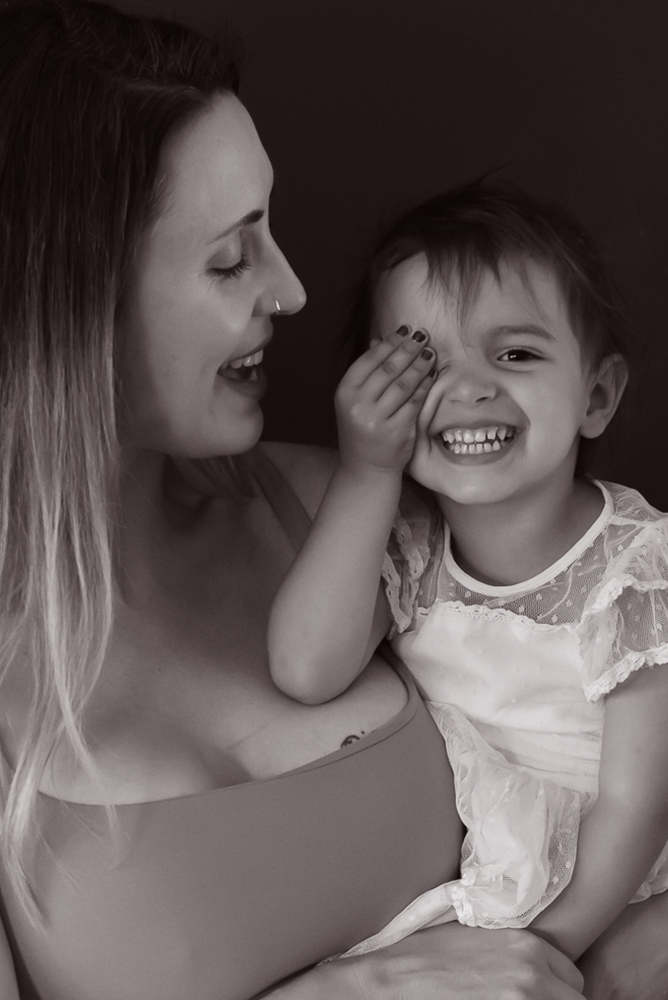 black and white portrait of mother and daughter who is smiling and covering her eye